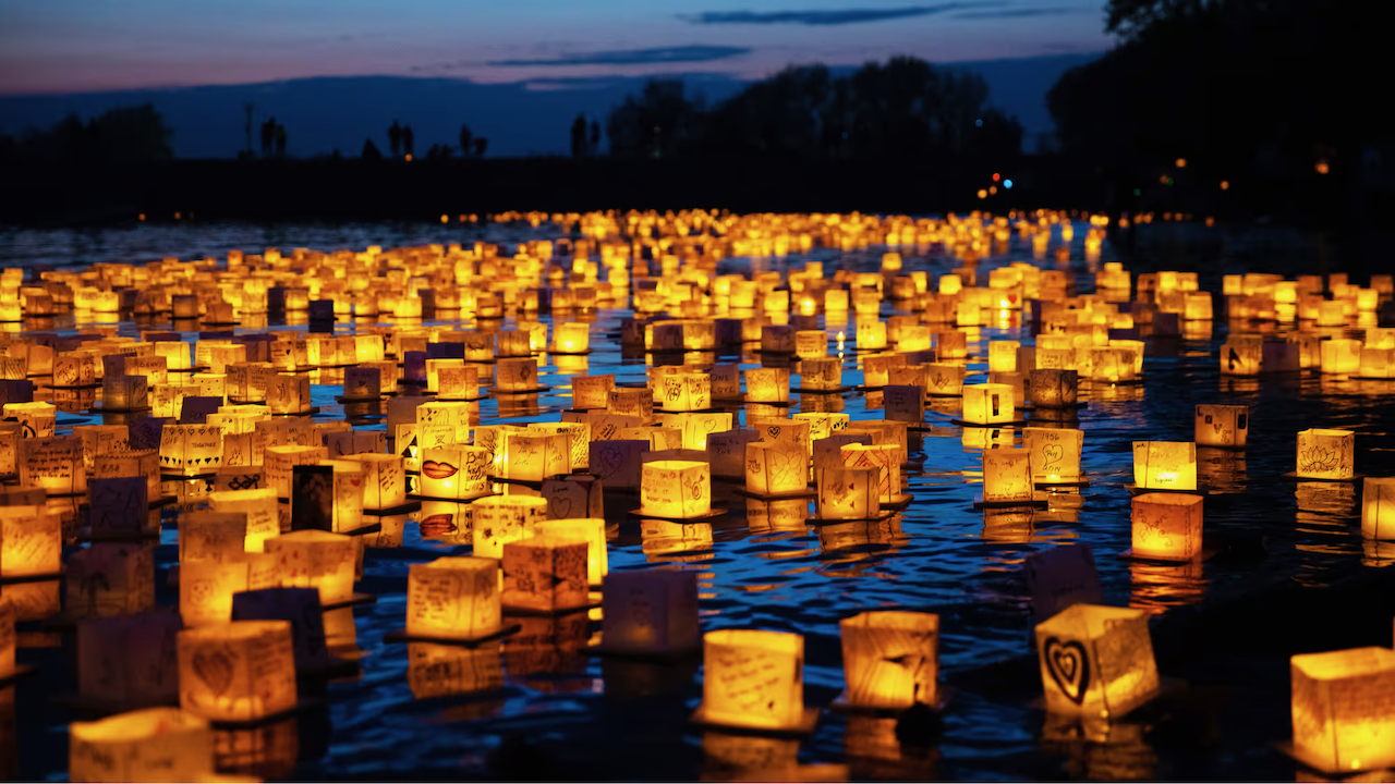 Hundreds of glowing paper lanterns decorated with hearts and handwritten messages float on the water at dusk.